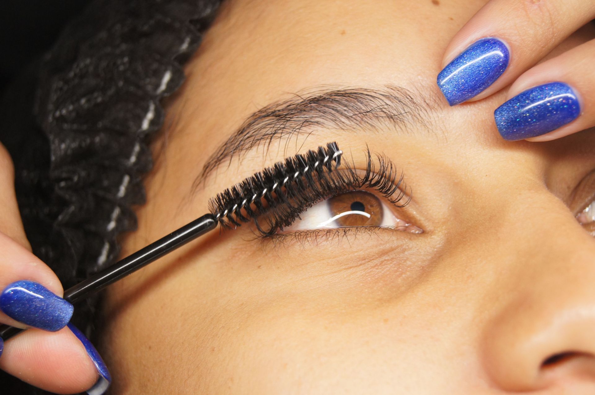 Detailed shot of eyelash extension application on a woman with blue painted nails.